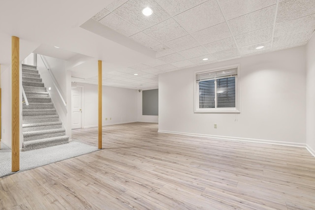 finished basement with light wood finished floors, baseboards, stairs, and a paneled ceiling