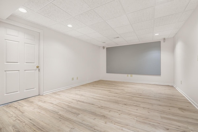 empty room with baseboards, a drop ceiling, and light wood-type flooring