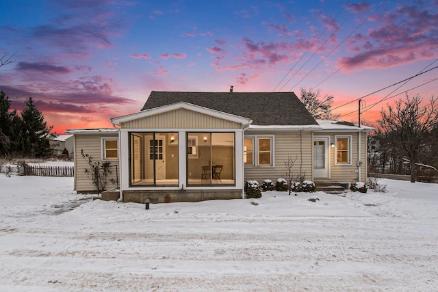 snow covered rear of property with a shingled roof and entry steps