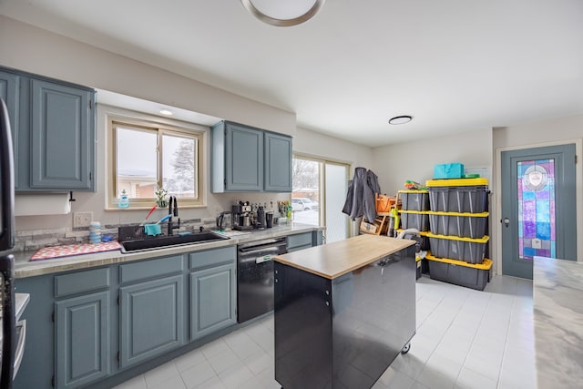 kitchen with black dishwasher, light countertops, a sink, and a center island