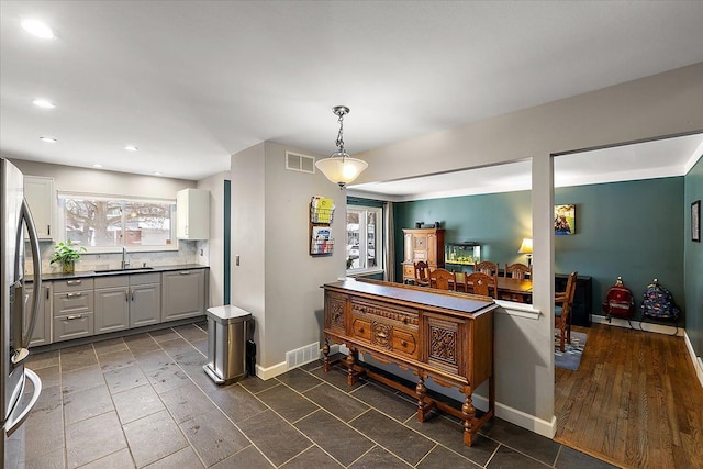 kitchen with hanging light fixtures, white cabinetry, a sink, and visible vents