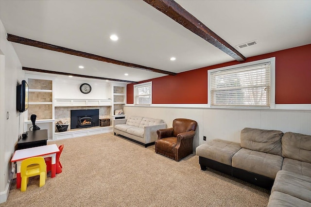 living room with a warm lit fireplace, light carpet, visible vents, wainscoting, and beamed ceiling