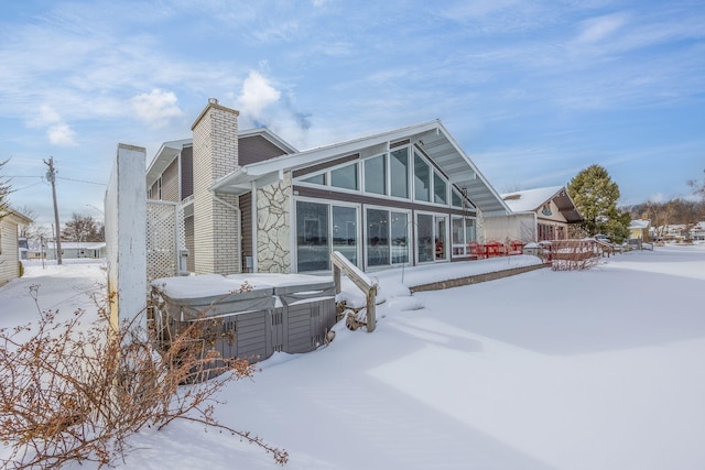 snow covered property featuring a hot tub and a chimney