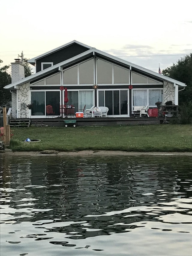 back of property with a yard, a water view, and a chimney