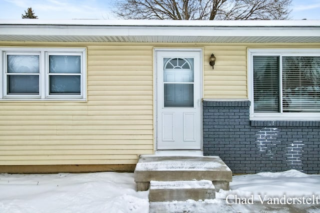 snow covered property entrance featuring brick siding