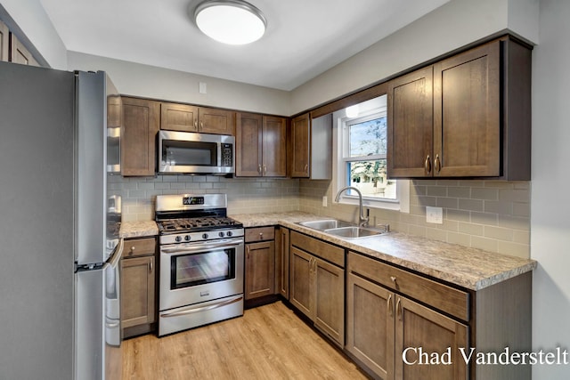 kitchen featuring stainless steel appliances, light wood-style flooring, decorative backsplash, and a sink