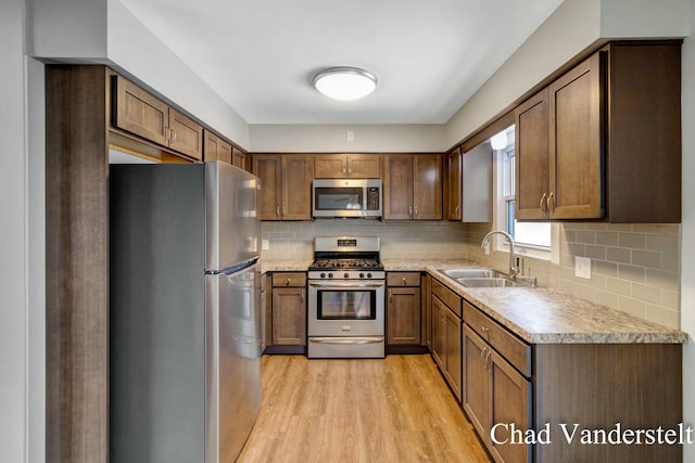 kitchen with light wood finished floors, a sink, tasteful backsplash, light countertops, and appliances with stainless steel finishes