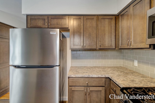 kitchen featuring stainless steel appliances, brown cabinetry, light countertops, and backsplash