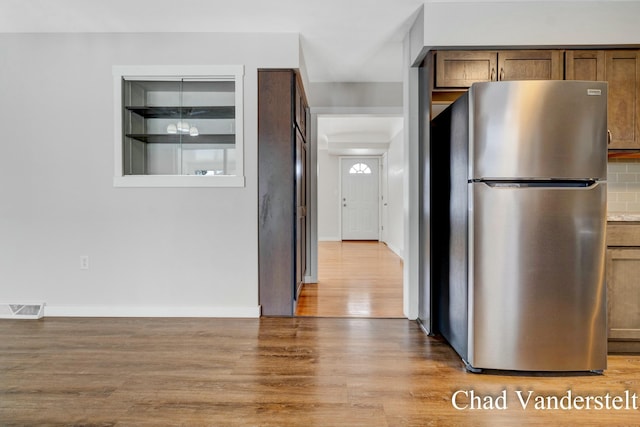 kitchen featuring freestanding refrigerator, visible vents, light wood finished floors, brown cabinets, and decorative backsplash