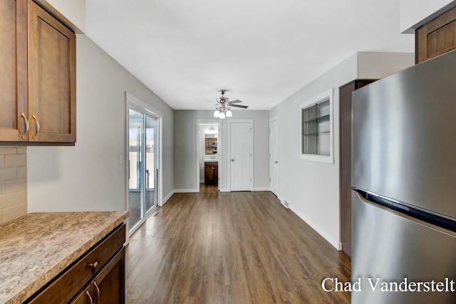 kitchen featuring dark wood-style floors, a ceiling fan, freestanding refrigerator, light countertops, and brown cabinetry