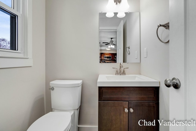 half bathroom with ceiling fan, vanity, and toilet