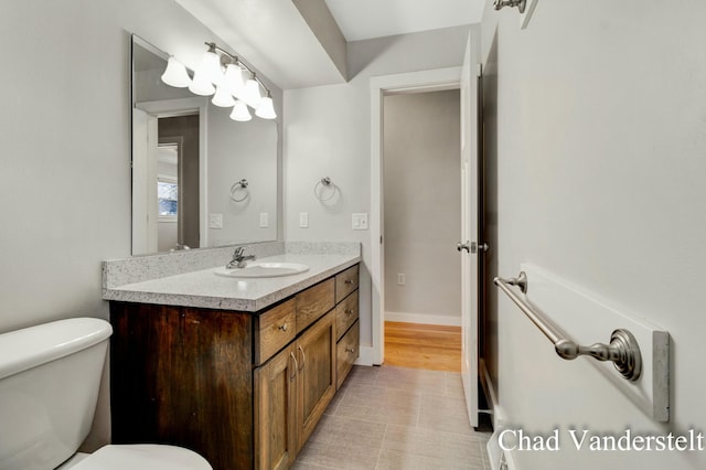 half bath featuring baseboards, vanity, and toilet