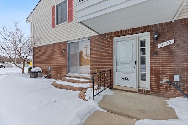 snow covered property entrance with brick siding