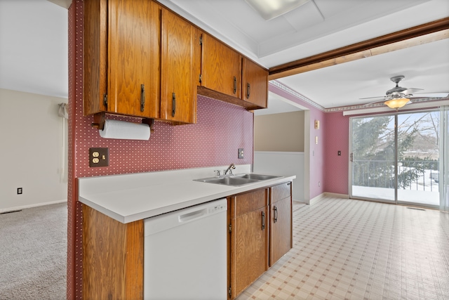 kitchen featuring brown cabinets, light countertops, white dishwasher, and a sink