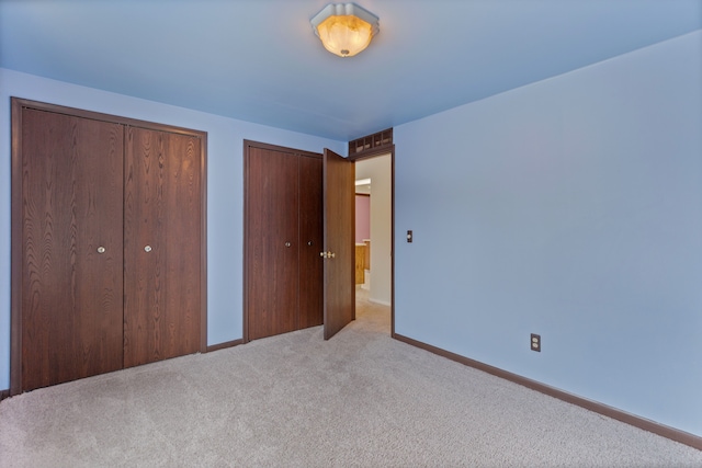 unfurnished bedroom featuring baseboards, two closets, and light colored carpet