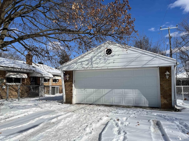 snow covered garage featuring a garage and fence