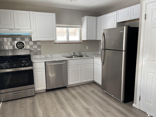 kitchen with light wood-style flooring, appliances with stainless steel finishes, under cabinet range hood, white cabinetry, and a sink