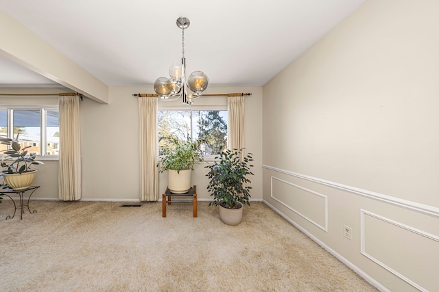 carpeted dining room with wainscoting, visible vents, a notable chandelier, and a decorative wall