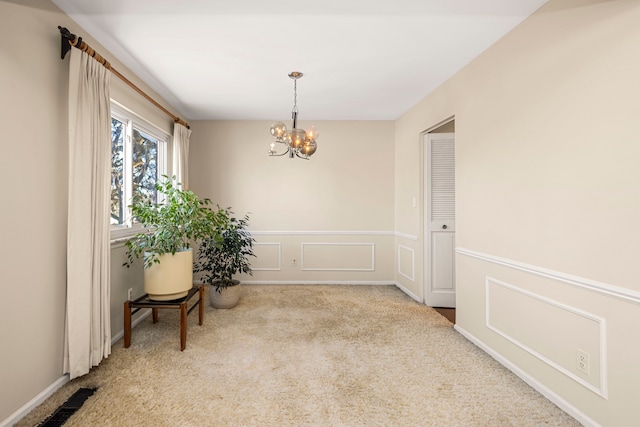 interior space with light carpet, visible vents, wainscoting, an inviting chandelier, and a decorative wall