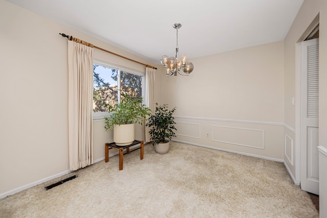 unfurnished room featuring visible vents, a wainscoted wall, an inviting chandelier, carpet floors, and a decorative wall