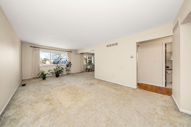 empty room with baseboards, visible vents, and light colored carpet