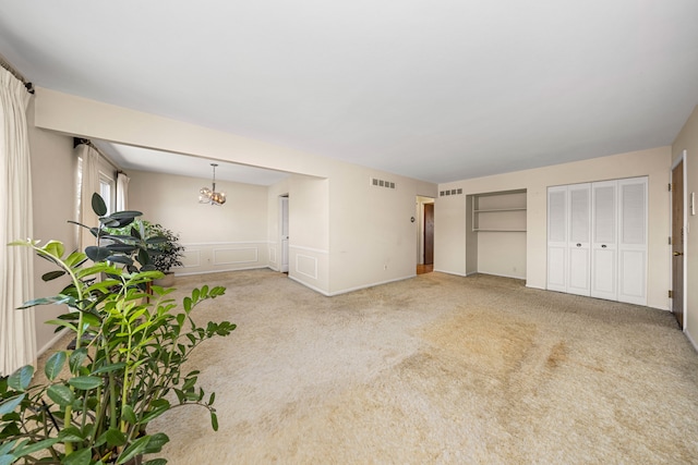 interior space with light carpet, a decorative wall, visible vents, and a notable chandelier