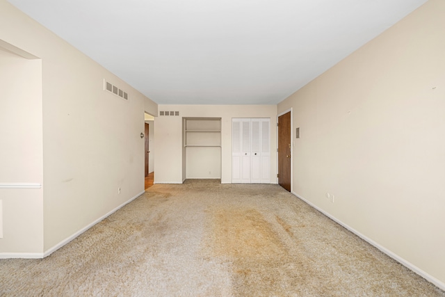 unfurnished bedroom with light carpet, baseboards, visible vents, and two closets