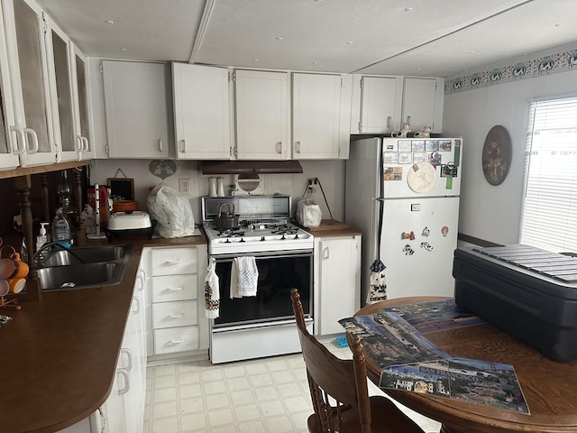 kitchen with white appliances, dark countertops, a sink, and white cabinets