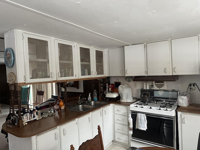 kitchen with white gas stove, dark countertops, glass insert cabinets, white cabinets, and a sink