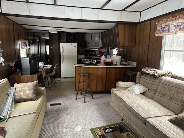 kitchen featuring dark brown cabinetry, wooden walls, a peninsula, light countertops, and freestanding refrigerator