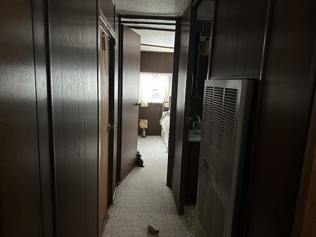 corridor featuring light colored carpet, wood walls, and a textured ceiling