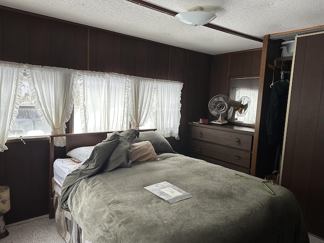 bedroom featuring light carpet, multiple windows, wood walls, and a textured ceiling