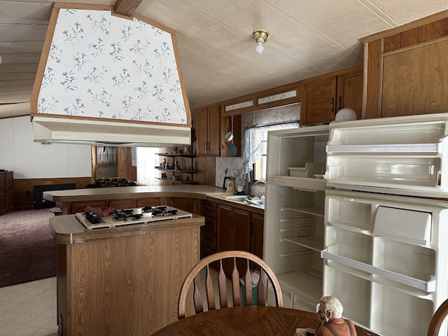 kitchen featuring custom exhaust hood, white gas stovetop, brown cabinetry, wainscoting, and a sink