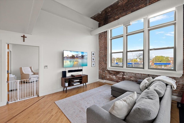 living room featuring brick wall, a high ceiling, wood finished floors, baseboards, and beam ceiling