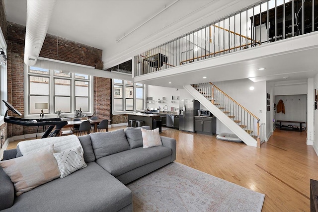 living area with brick wall, a towering ceiling, light wood finished floors, and stairs