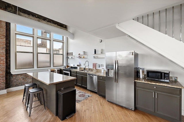 kitchen featuring light stone countertops, stainless steel appliances, a sink, a center island, and open shelves