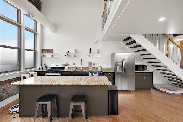 kitchen with appliances with stainless steel finishes, a sink, light stone counters, and a kitchen bar