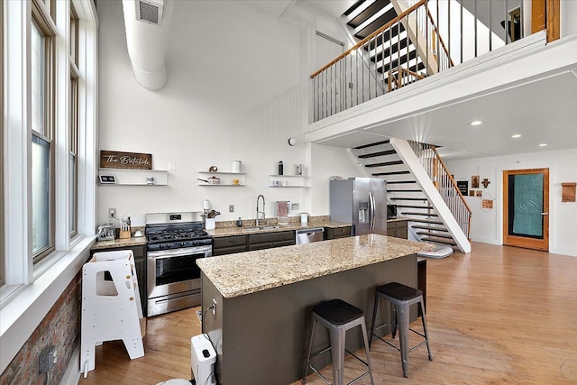 kitchen featuring visible vents, a towering ceiling, appliances with stainless steel finishes, a center island, and open shelves