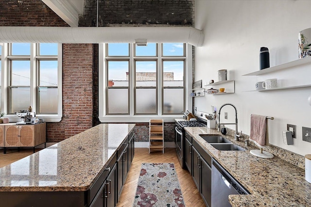 kitchen featuring stainless steel appliances, light stone countertops, a sink, brick wall, and an island with sink