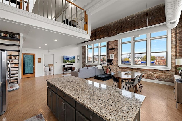 kitchen featuring light wood-style flooring, a high ceiling, open floor plan, a kitchen island, and brick wall