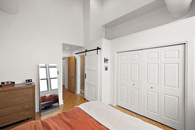 bedroom featuring a barn door, light wood-style flooring, a high ceiling, baseboards, and a closet