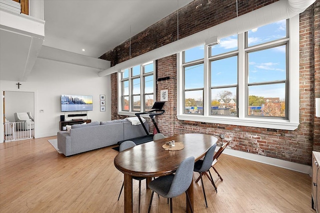 dining space with light wood-style floors, brick wall, a high ceiling, and baseboards