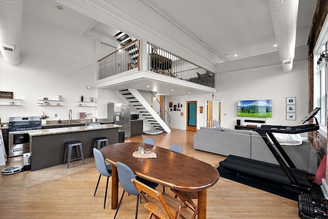 dining space with stairs, light wood finished floors, and a towering ceiling