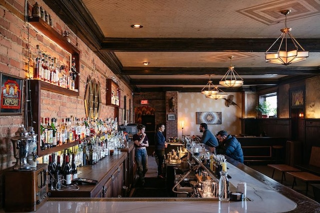 bar with brick wall, a bar, beamed ceiling, and pendant lighting