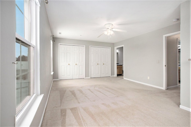 unfurnished bedroom with a ceiling fan, light carpet, baseboards, and two closets