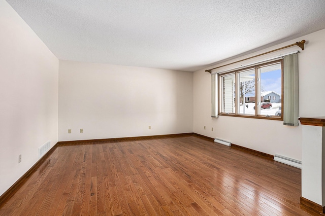 spare room featuring a baseboard radiator, visible vents, a textured ceiling, wood finished floors, and baseboards