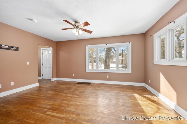 spare room with visible vents, wood finished floors, a ceiling fan, and baseboards