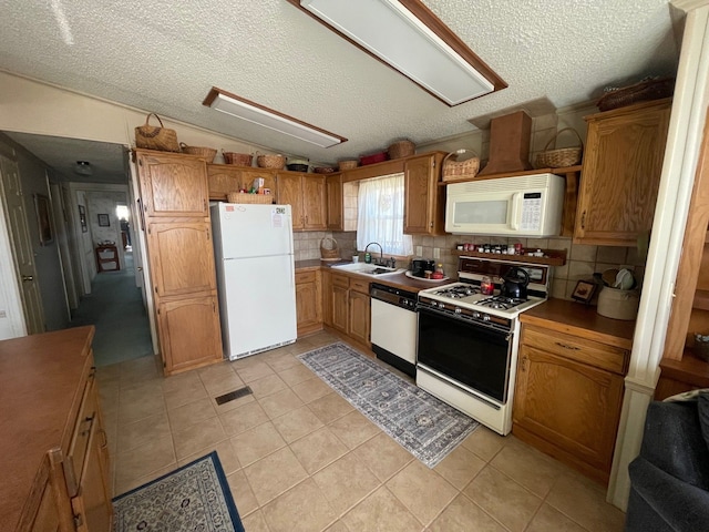 kitchen with light tile patterned flooring, white appliances, a sink, visible vents, and vaulted ceiling