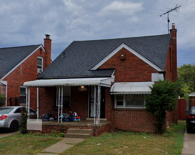 view of front facade with a shingled roof, a front lawn, a chimney, and brick siding