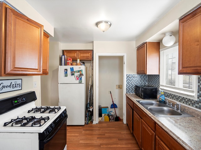 kitchen featuring brown cabinetry, freestanding refrigerator, black microwave, a sink, and gas stove